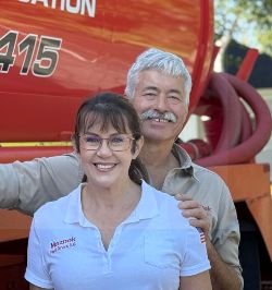 Man and woman in blue work shirts standing next to orange septic tank truck