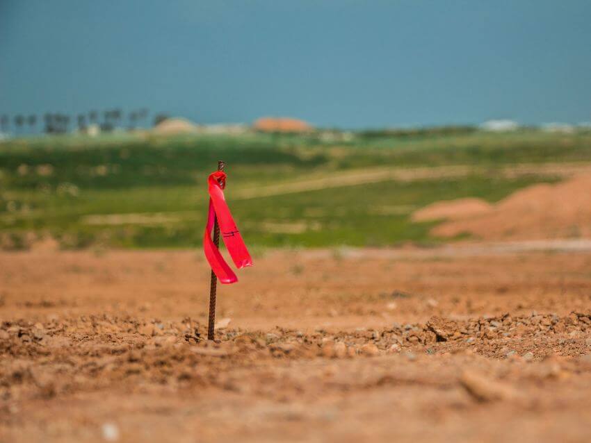 Wood stake with red ribbon tied to it in middle of dirty grass area
